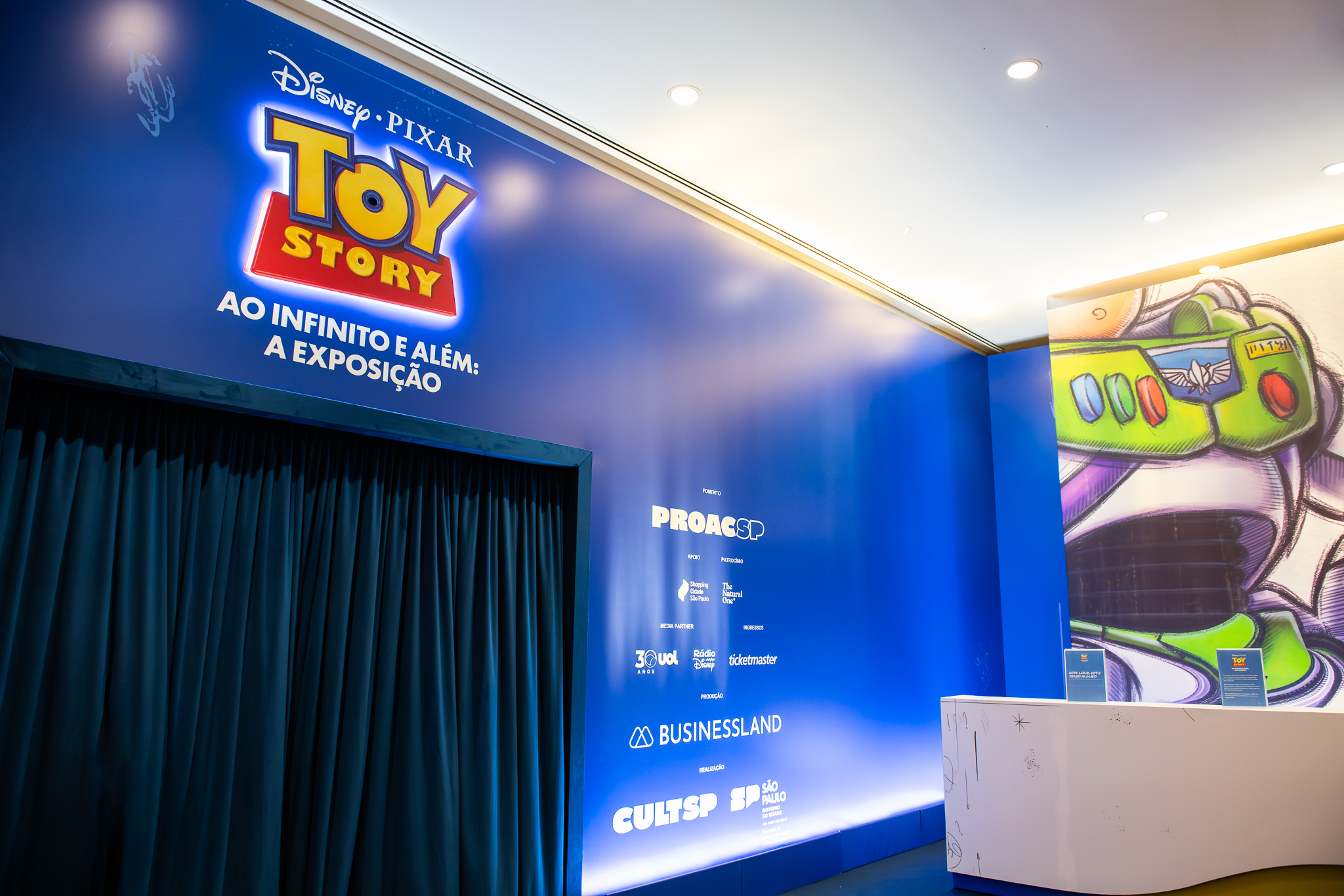 Entrada da exposição Toy Story Ao Infinito e Além no Shopping Cidade São Paulo com logo Disney Pixar iluminado e ilustração do Buzz Lightyear