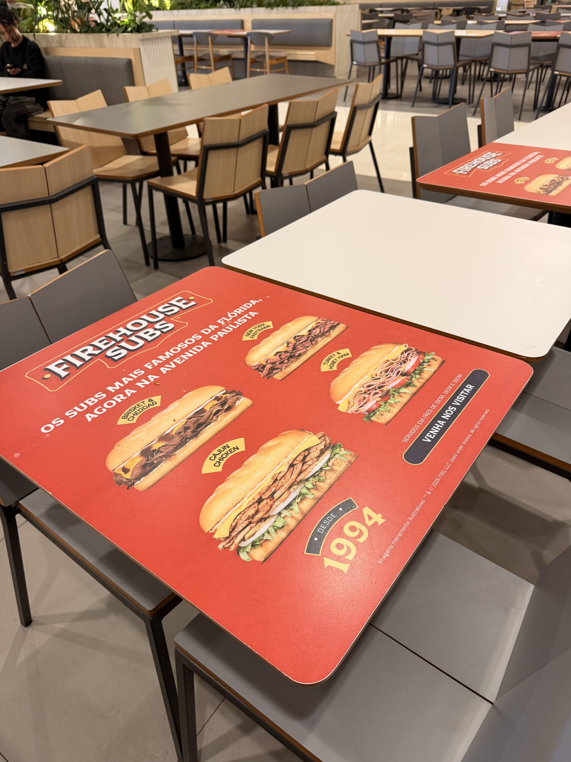 Mídia OOH em adesivo de mesa de praça de alimentação de shopping com campanha Firehouse Subs Avenida Paulista