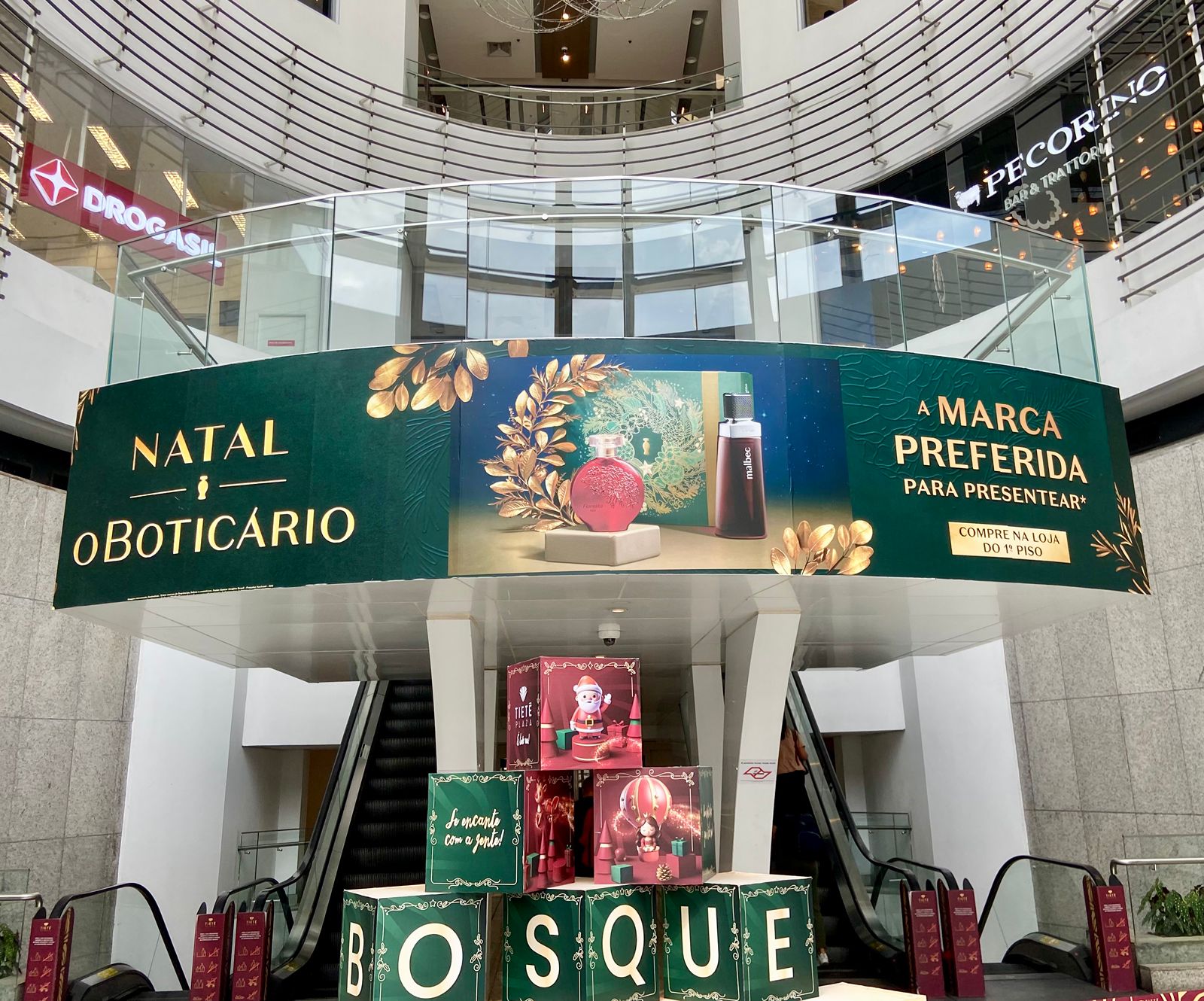 Mídia indoor em painel curvo de balcão de shopping com campanha de Natal O Boticário Malbec