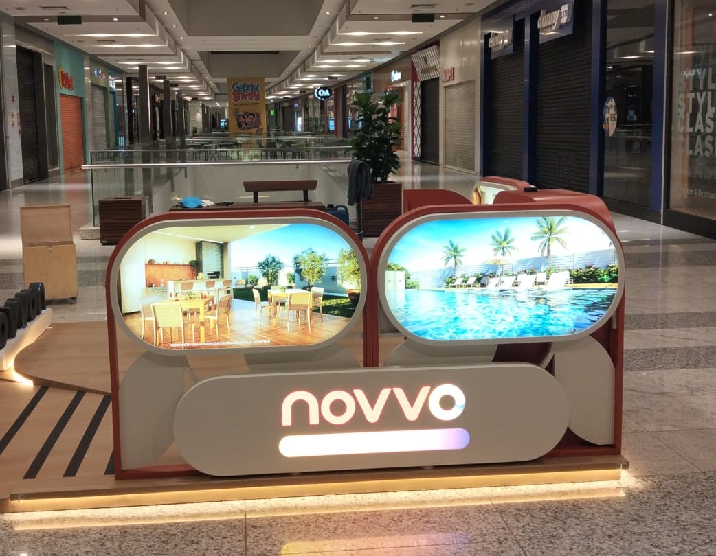 Stand imobiliário Novvo no corredor de shopping center com painéis iluminados exibindo área de lazer e piscina de empreendimento residencial