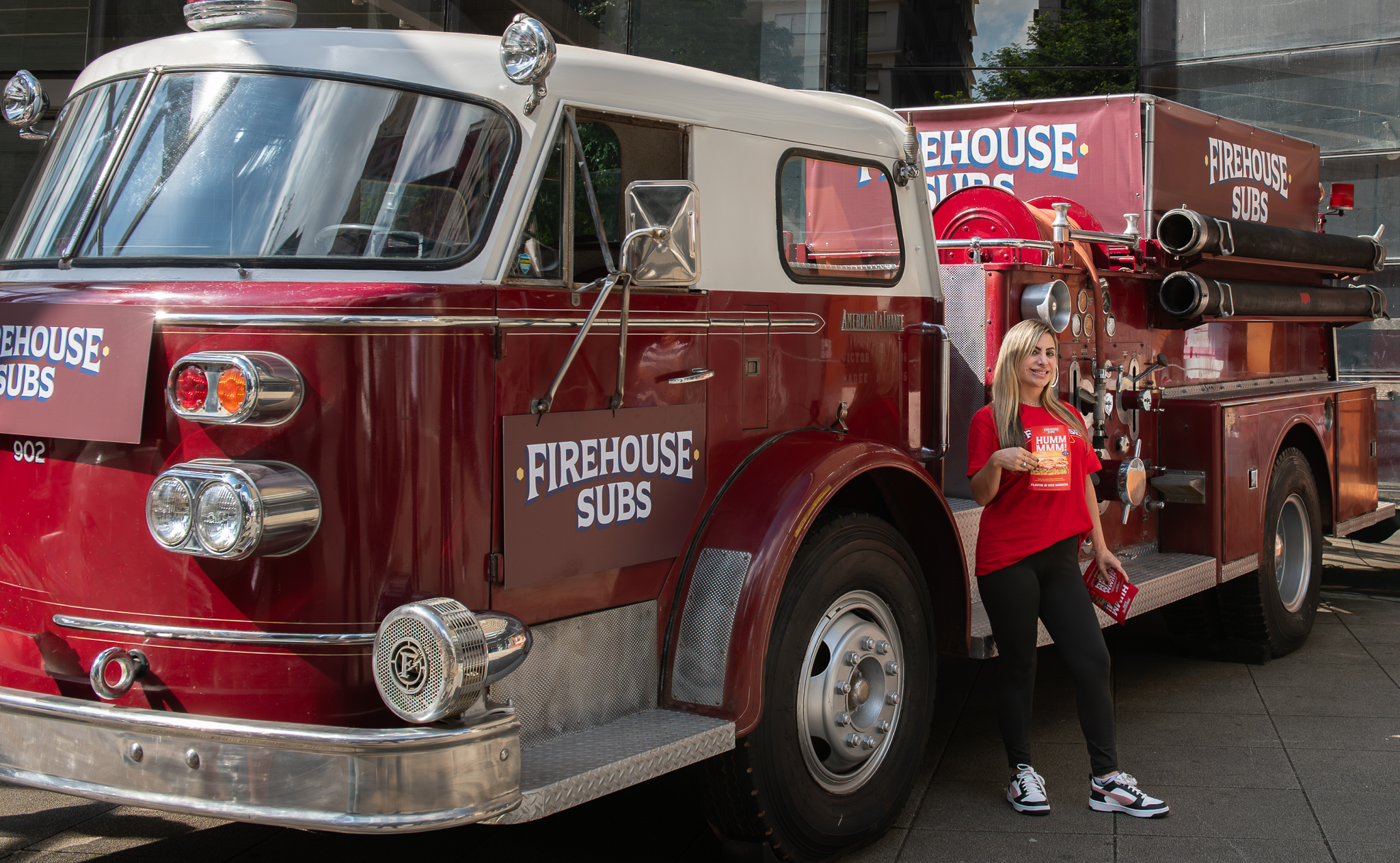 Promotora da Firehouse Subs ao lado de caminhão de bombeiros temático em ativação na Avenida Paulista.