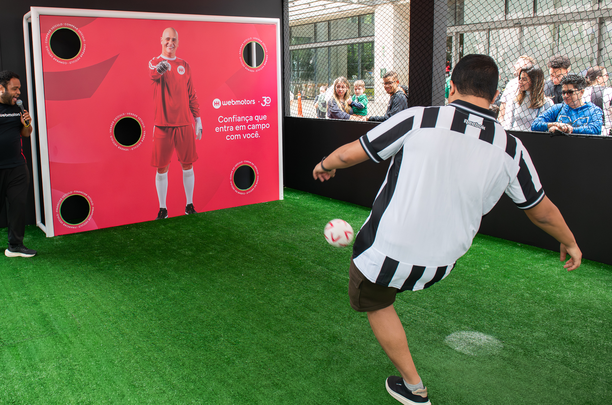 Consumidor chutando bola em ativação interativa da Webmotors com campo de futebol em shopping center.